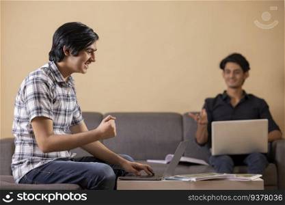 Two happy teenage boys doing homework at home using laptop