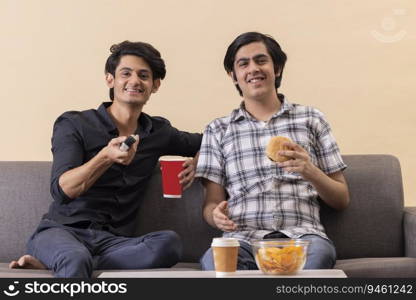 Two happy teenage boys eating fast foods and watching TV together at home