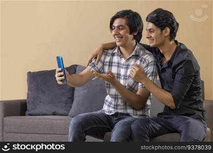 Two happy teenage boys having a video call on smartphone at home