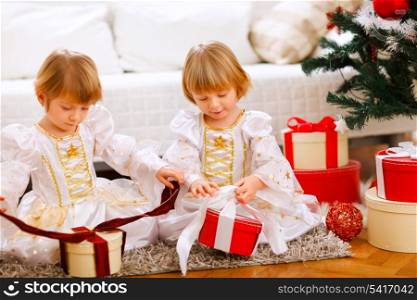 Two happy twins girl opening presents near Christmas tree&#xA;