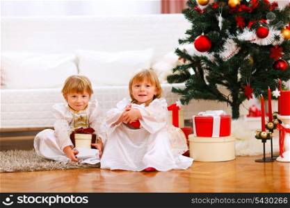 Two happy twins girl sitting with presents under Christmas tree&#xA;