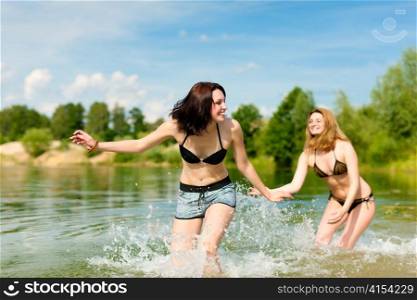 Two happy women having fun in summer at lake; they wearing swimwear