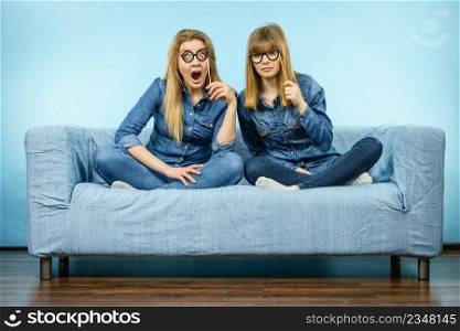 Two happy women holding fake eyeglasses on stick having shocked face expression wearing jeans shirts. Photo and carnival funny accessories concept.. Two shocked women holding fake eyeglasses on stick