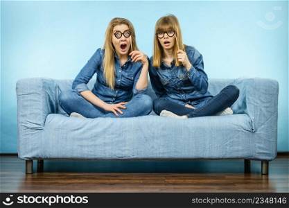 Two happy women holding fake eyeglasses on stick having shocked face expression wearing jeans shirts. Photo and carnival funny accessories concept.. Two shocked women holding fake eyeglasses on stick