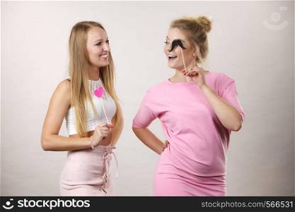 Two happy women holding symbols on stick having fun. Photo and carnival funny accessories concept.. Two women holding carnival accessories