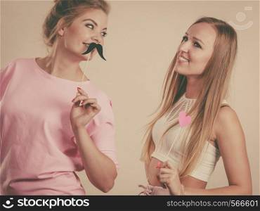 Two happy women holding symbols on stick having fun. Photo and carnival funny accessories concept.. Two women holding carnival accessories
