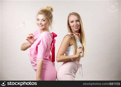 Two happy women holding symbols on stick having fun pretending to wear eyeglasses. Photo and carnival funny accessories concept.. Two women holding carnival accessories