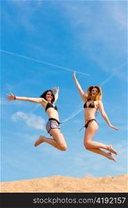 Two happy women jumping high in summer with fun with the blue sky in the background