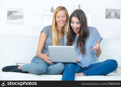 two happy young friends with laptop at home