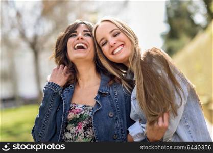 Two happy young women friends hugging in the street. Blonde and brunette girls wearing casual clothes outdoors.