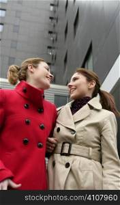 Two happy young women with winter coats, black building background