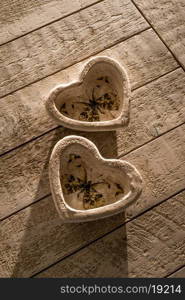 Two heart decorations on a white whashed wooden table in low directional light of the late afternoon.