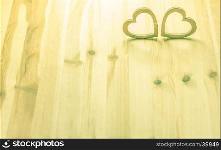Two hearts, hand carved from wood, in a warm light on a wooden background