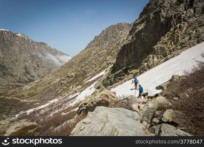 Two hikers and two dogs traversing the snow in the mountains of Restonica near Lac de Melo