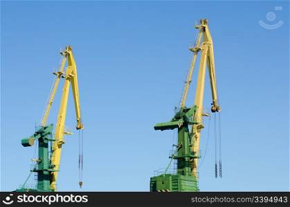 two hoisting cranes against clear blue sky