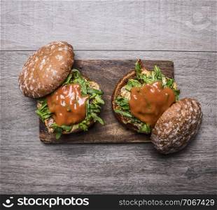 two home burgers with chicken in mustard sauce, arugula, tomatoes on a cutting board on wooden rustic background top view close up