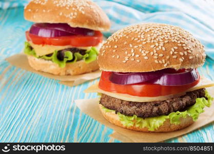 Two homemade cheeseburgers with beef patties and fresh salad on seasame buns, served on blue wooden table.. Homemade cheeseburger on blue wooden surface.