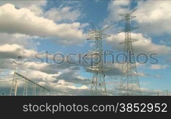 Two huge electrical towers with workers and clouds going by.Four workers are assembling the towers at the beginning of the power line.Electrical towers are an icon of our time.Suitable for development, technification, evolution, progress, future
