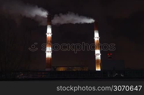 Two huge smoking factory pipes illuminated at night. Industry, manufacture and air pollution in the city