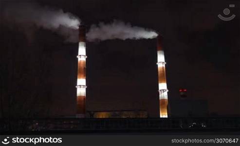 Two huge smoking factory pipes illuminated at night. Industry, manufacture and air pollution in the city