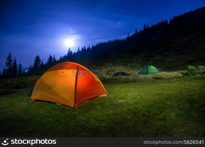 Two Illuminated orange and green camping tents under moon, stars at night