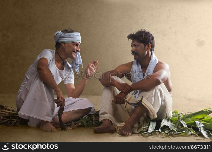 Two Indian farmer holding farming tools and talking