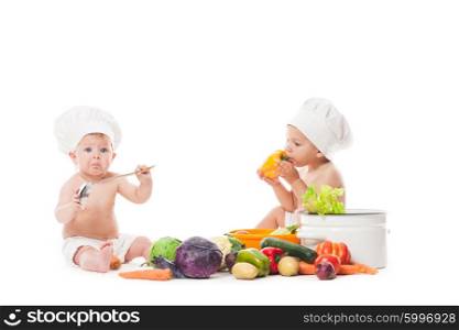 Two infant kids play with vegatables. Babies in chef hats isolated on white. Little chefs cook