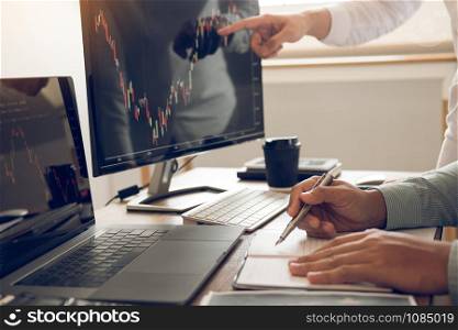 Two investors are working together with analyzing the stock data graphs in the paper and viewing the data on the laptop screen.