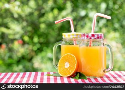 Two jars of orange juice and half an orange. Natural green background. Two jars of orange juice and half an orange