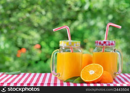 Two jars of orange juice and half orange leaves. Natural green background. Two jars of orange juice and half orange leaves