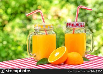 Two jars of orange juice on a red checkered tablecloth. Natural green background. Two jars of orange juice on red checkered tablecloth