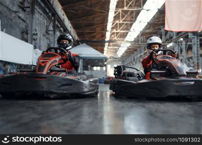 Two kart racers fight for victory on lap, side view, karting auto sport indoor. Speed race on close go-cart track with tire barrier. Fast vehicle competition. Two kart racers fight for victory, side view