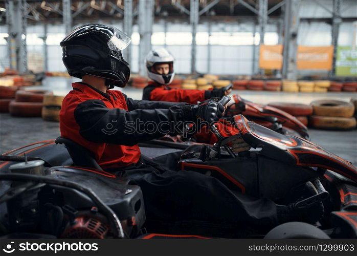 Two kart racers fight for victory on lap, side view, karting auto sport indoor. Speed race on close go-cart track with tire barrier. Fast vehicle competition, high adrenaline leisure