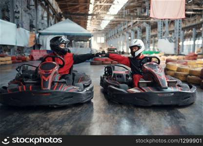 Two kart racers on start line, front view, karting auto sport indoor. Speed race on close go-cart track with tire barrier. Fast vehicle competition, high adrenaline leisure