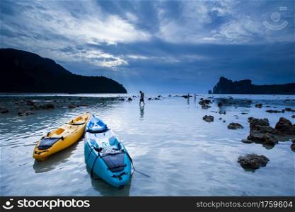 Two kayak and tourists relaxing on the rock beach at dusk, fantastic blue clouds over Andaman Sea backdrop, serene seascape at Phuket Island, top tourist attraction in Thailand.