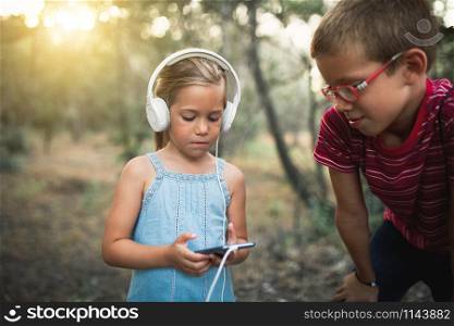Two kids listening to music in the forest with headphones