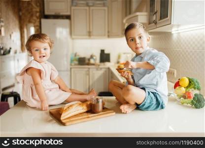 Two kids smears melted chocolate on bread, tasty sandwiches. Cute boy and girl cooking on the kitchen. Happy children prepares and tastes sweet dessert at the counter