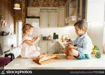 Two kids smears melted chocolate on bread, tasty sandwiches. Cute boy and girl cooking on the kitchen. Happy children prepares and tastes sweet dessert at the counter. Kids smears melted chocolate on bread