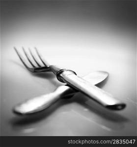 Two. Knife and fork over glass with reflection and shadow