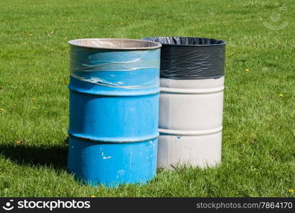 Two large blue and gray garbage bins on green grass with garbage bags inside.