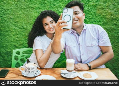 Two latin friends enjoying a coffee and taking a selfie. Happy latin friends having a coffee and taking a selfie