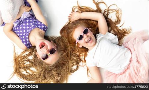 Two laughing kids lying on a white floor