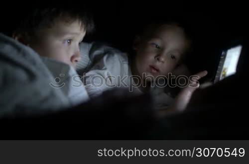 Two little boys in bed try to watch the film at night using the tablet