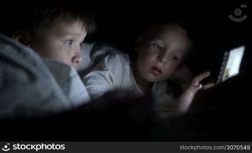 Two little boys in bed try to watch the film at night using the tablet