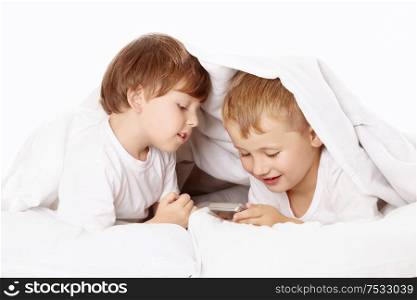 Two little boys secretly under a blanket play with a mobile phone