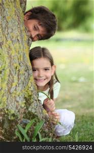 Two little children hiding behind tree