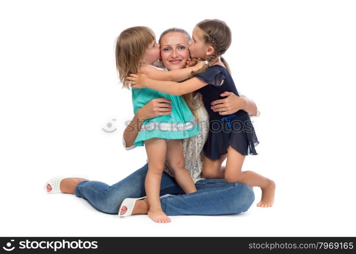 Two little daughters kiss Mom in the studio on a white background.