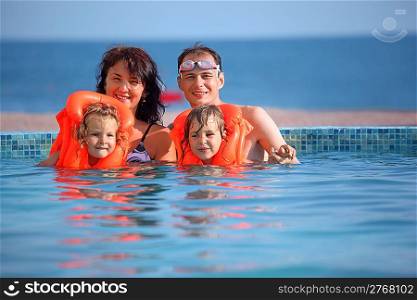two little girls bathing in lifejackets with parents in pool on resort, near ledge