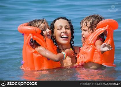 two little girls bathing in lifejackets with young woman in pool on resort