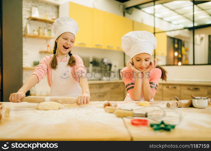 Two little girls chefs are laughing at each other, cookies preparation on the kitchen. Kids cooking pastry and having fun, children preparing cake. Two little girls chefs are laughing at each other